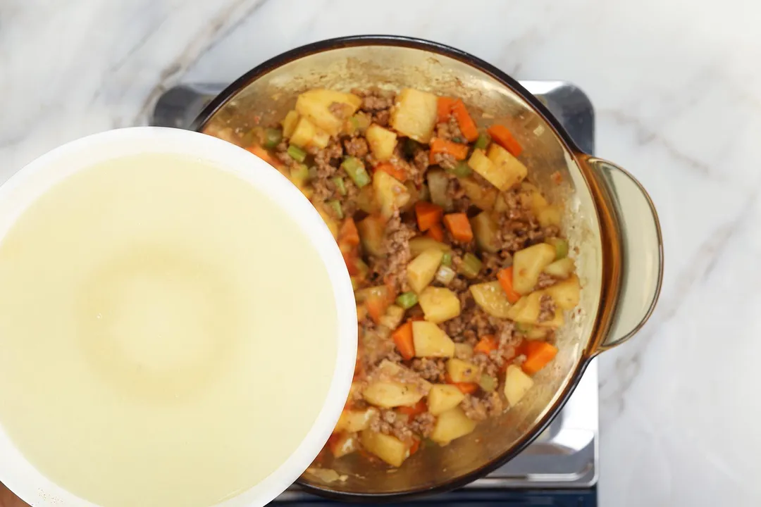 a bowl of broth on top of a pot of cooked ground beef and vegetables