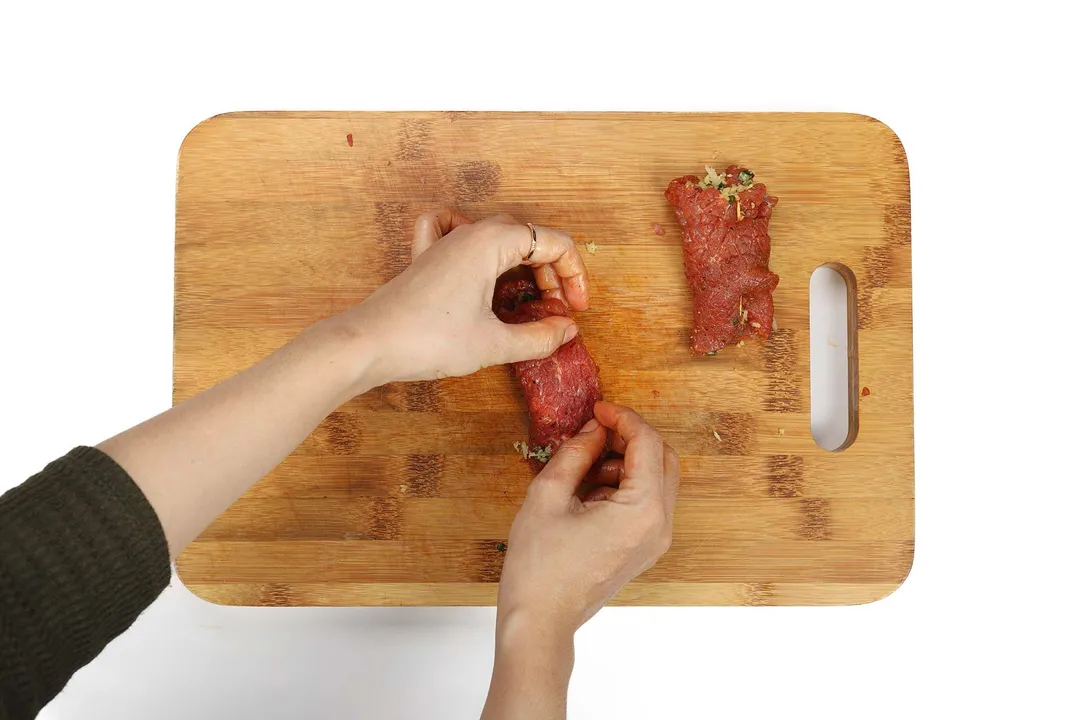 rolling beef braciole on a cutting board