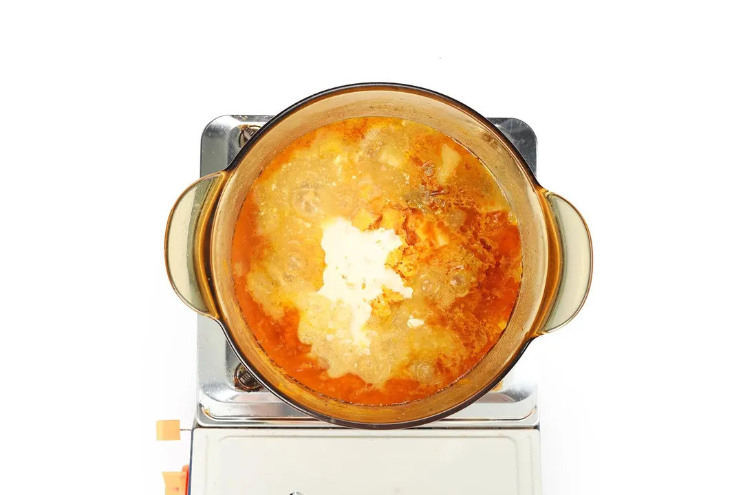 A glass saucepan filled with heavy cream, milk, and a soup cooking on a portable gas stove