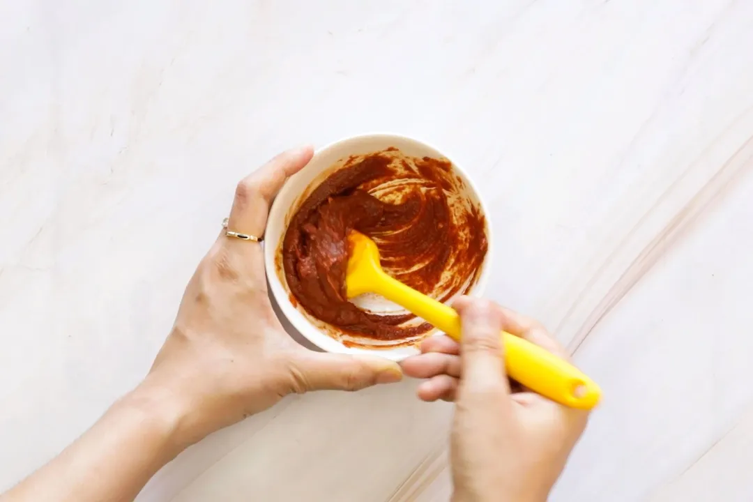 a hand using a wooden spoon to mix spicy in a small bowl