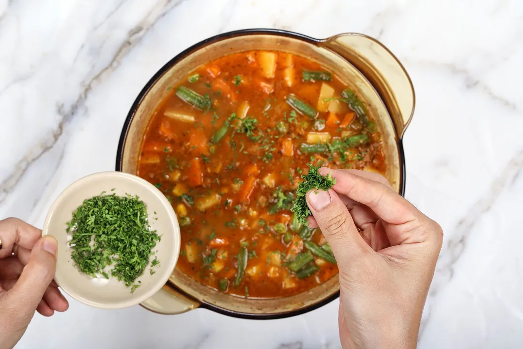 sprinkle chopped parsley from a small bowl onto a pot of soup