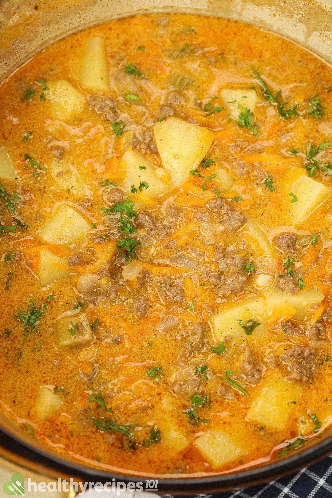 A saucepan filled with cooked potato cubes, ground beef, chopped parsley, and a thick dark yellow broth