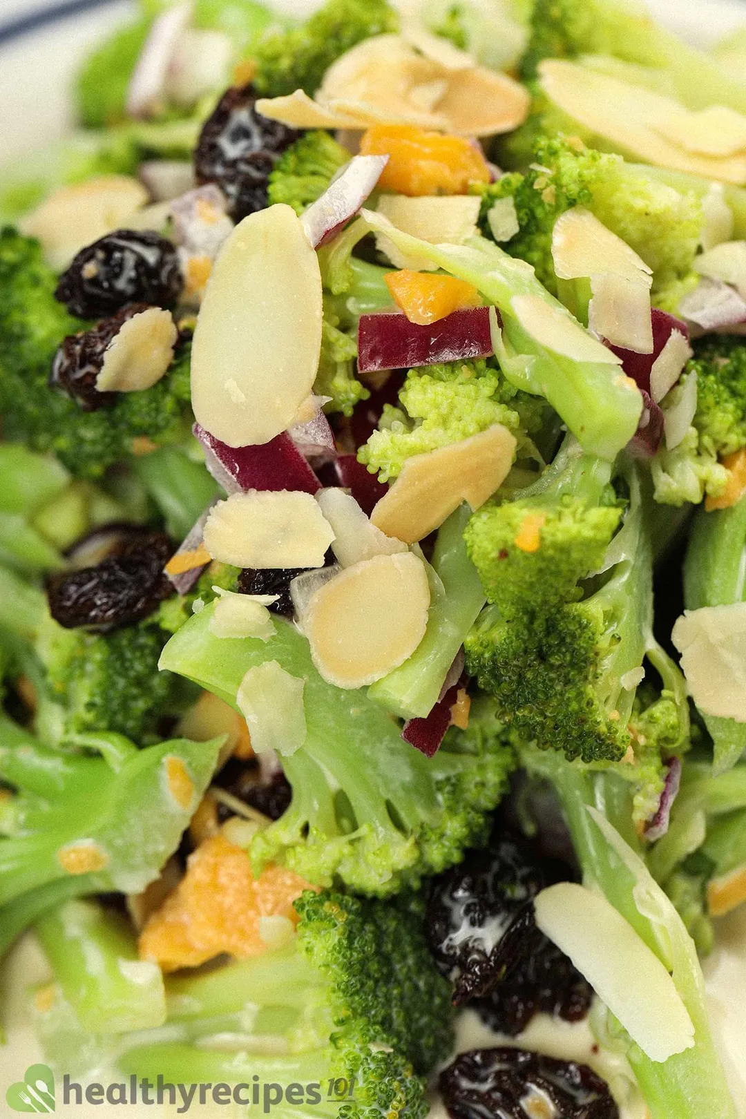 A close-up shot of a broccoli raisin salad, consisting of broccoli florets, raisins, sliced almond, and diced red onion