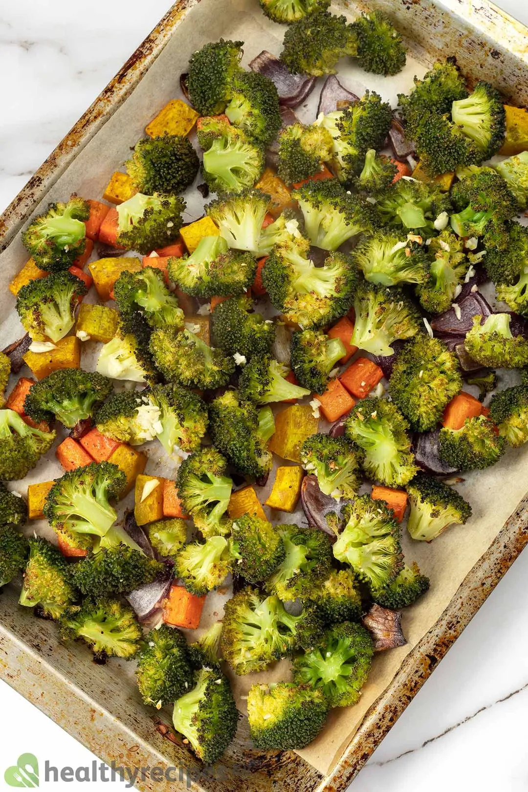 A high-angle shot of a sheetpan lined with parchment paper and filled with broccoli florets and squash cubes.