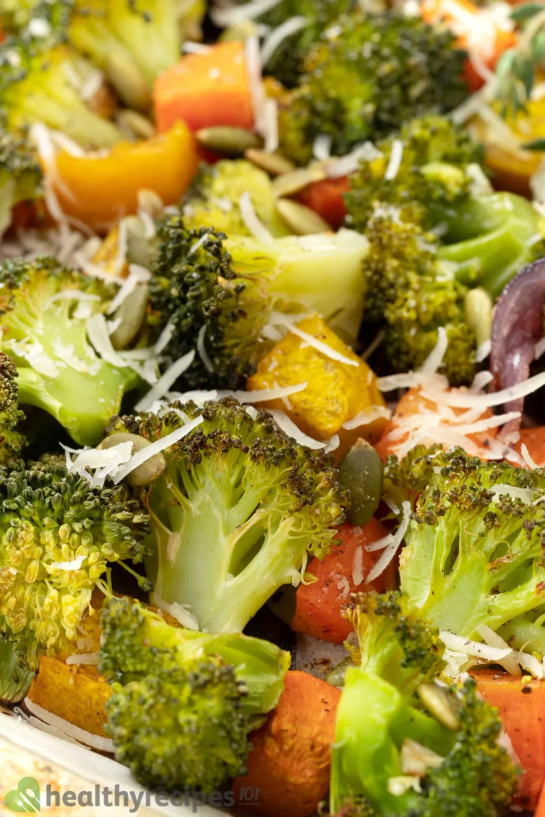 A close-up shot of roasted broccoli, squash cubes, and shredded cheese.