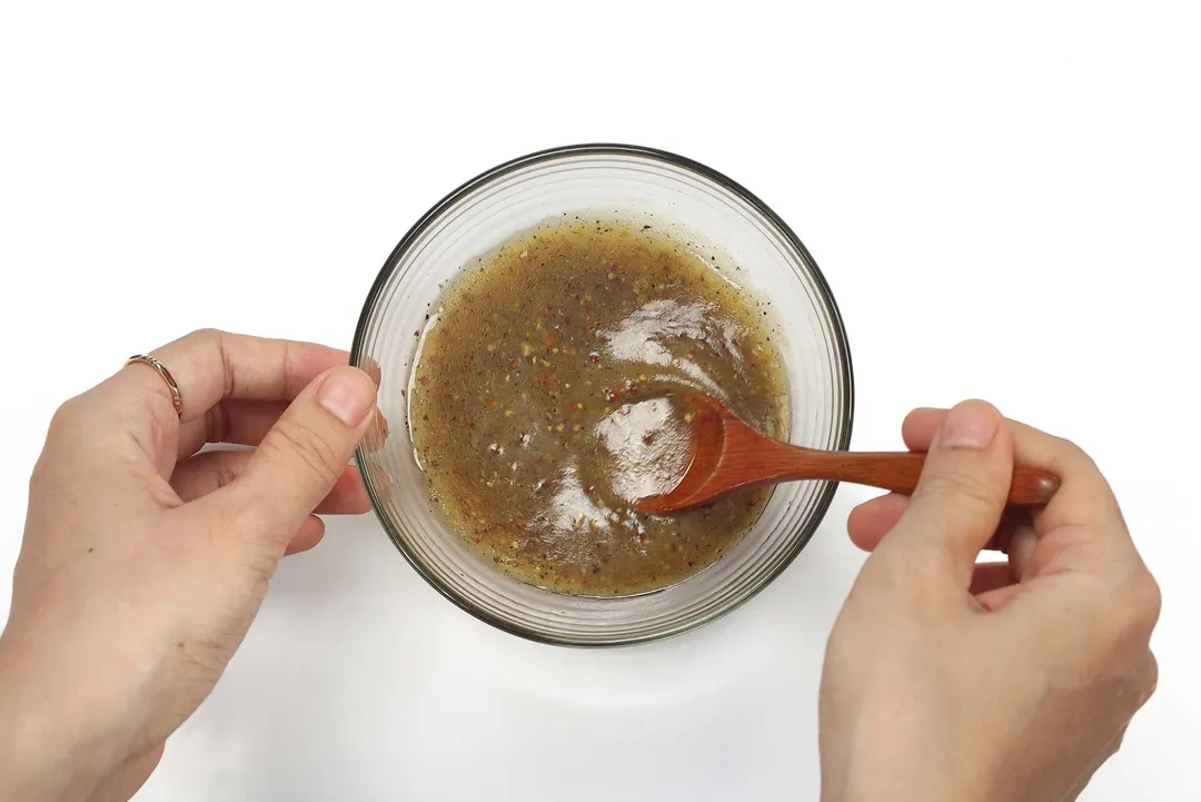 Two hands using a wooden spoon to mix a dressing in a small bowl