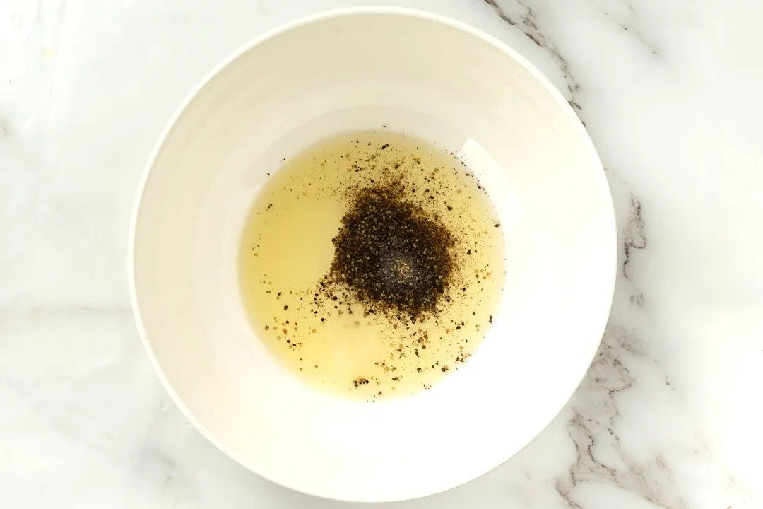 A white plate containing olive oil and ground black pepper.