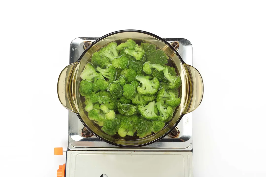 A saucepan cooking broccoli florets on a portable gas stove.