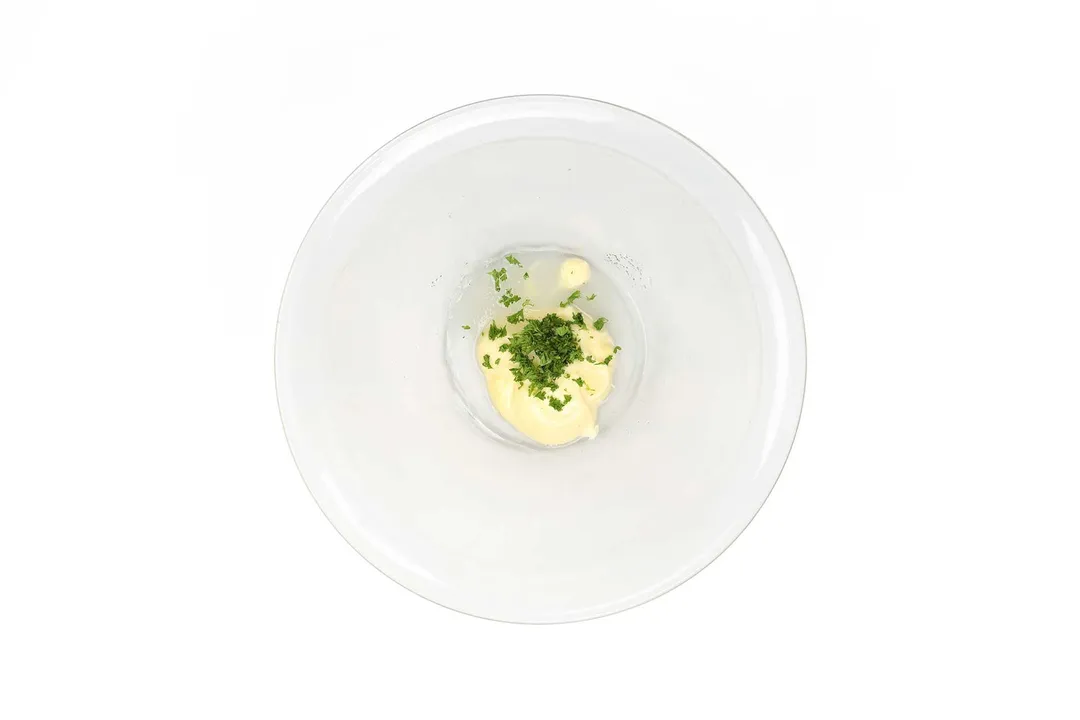 A glass bowl contains small dollops of mayonnaise and chopped parsley