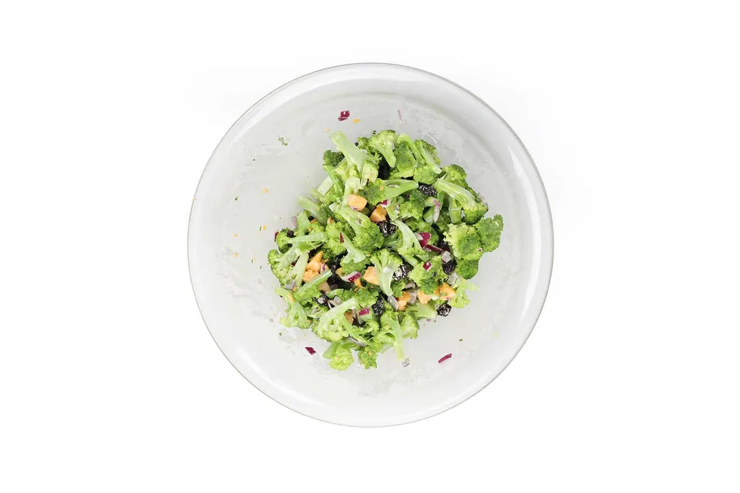 A glass bowl containing broccoli florets, slice almonds, and raisins