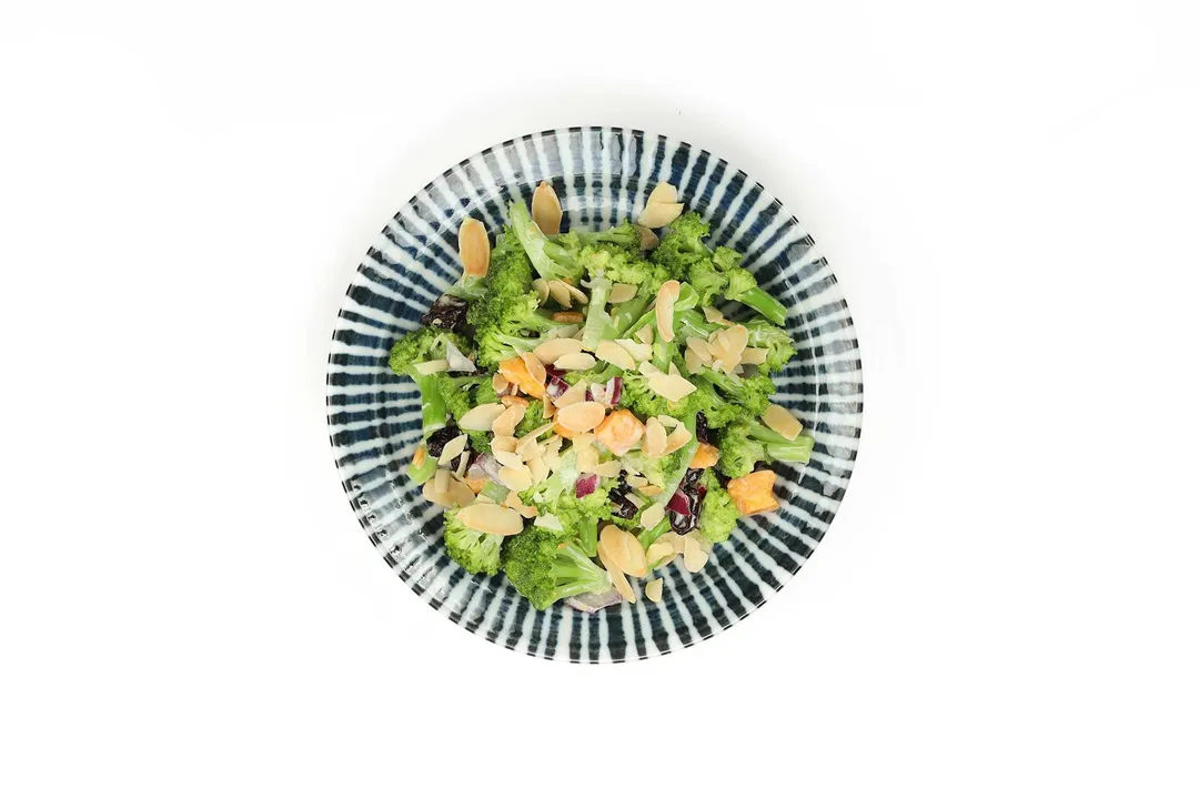 A blue and white stripe plate containing broccoli florets, slice almonds, and raisins