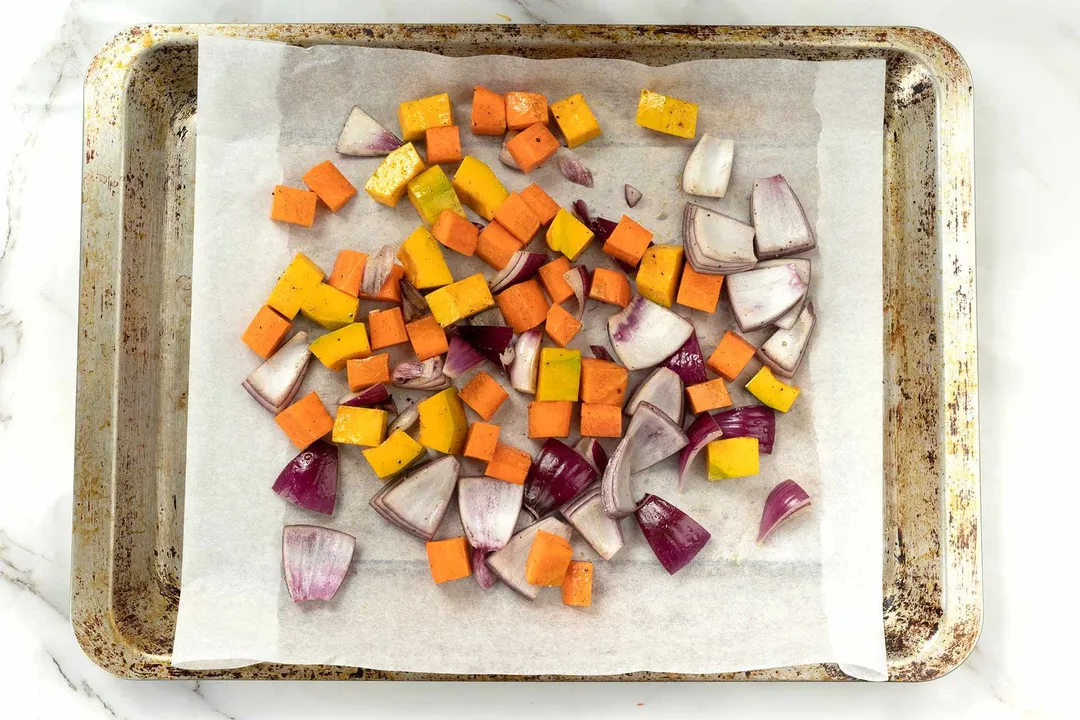 Cubed red onions and squash spread out on a sheetpan lined with parchment paper.