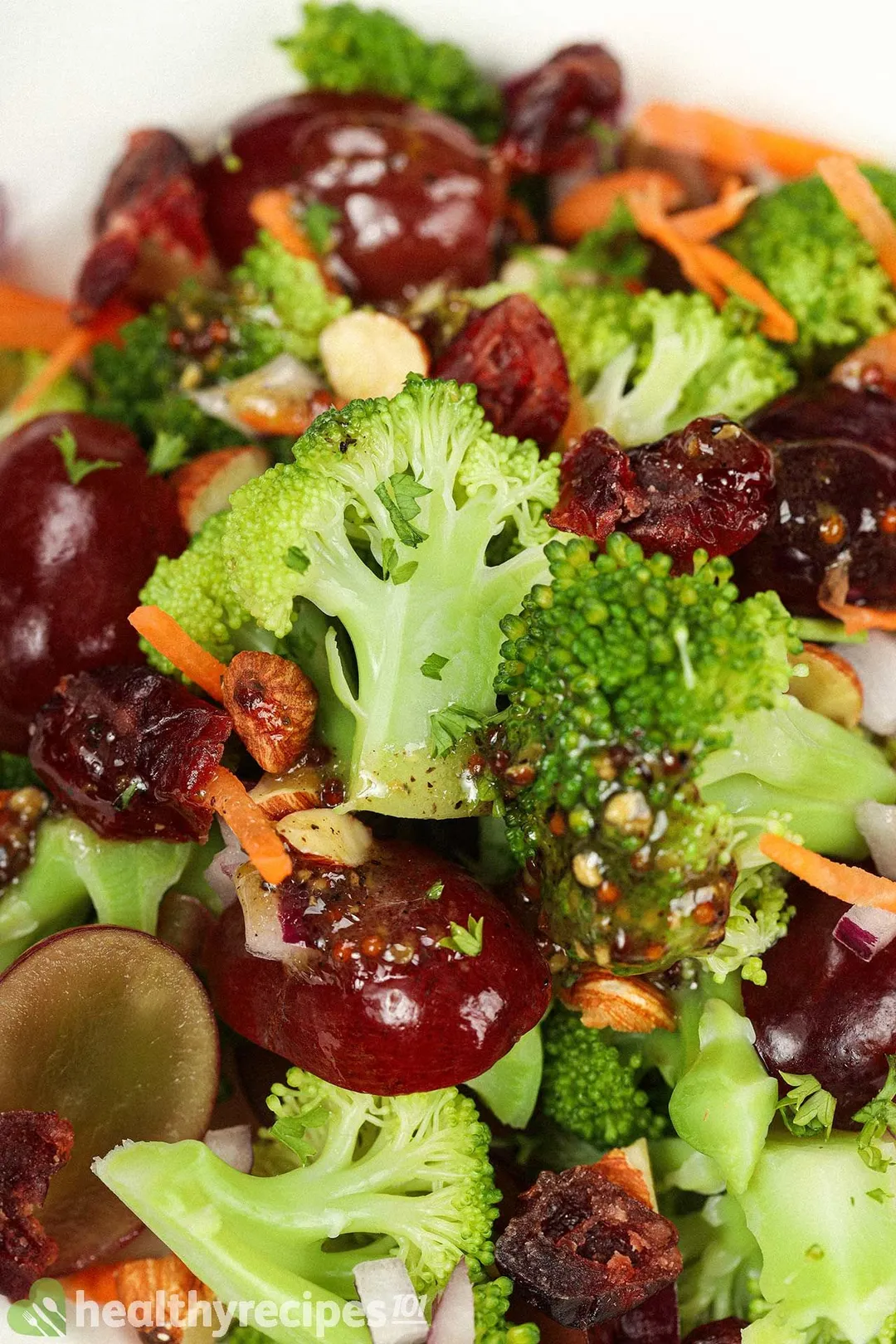 A close-up shot of vegan broccoli salad, including broccoli florets, red grapes, and carrot strips.
