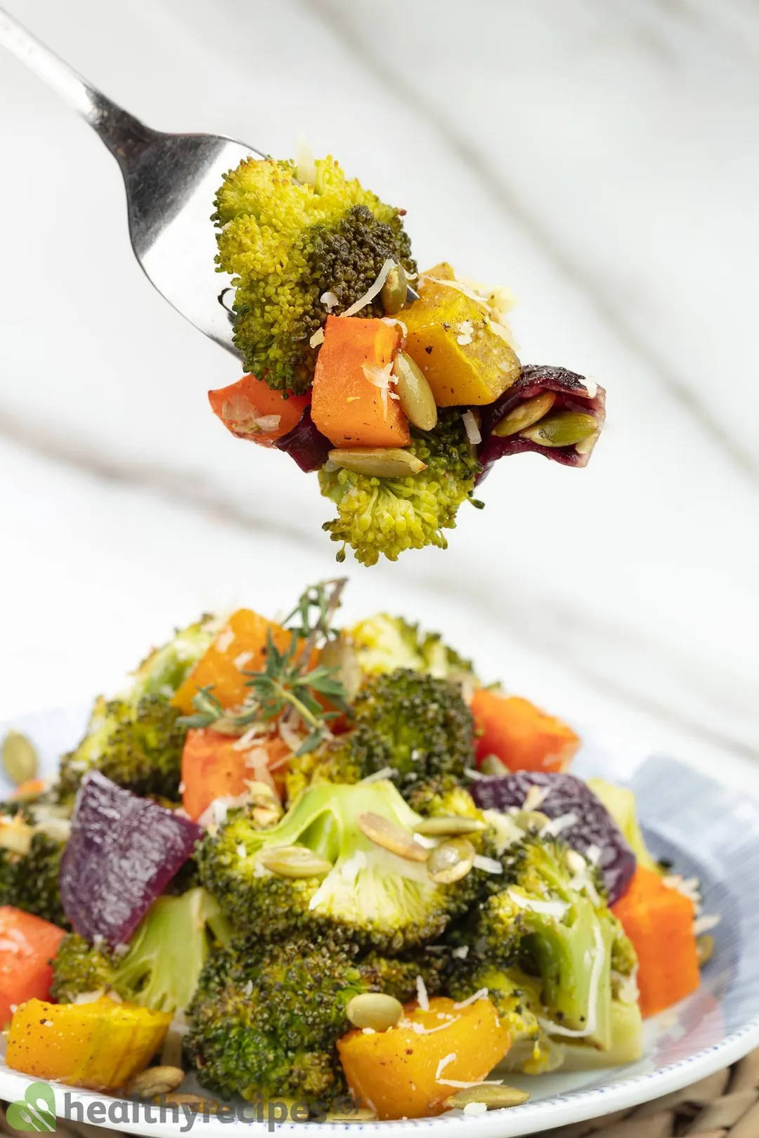 A fork picking up broccoli florets and squash cubes from a plate of roasted vegetables.