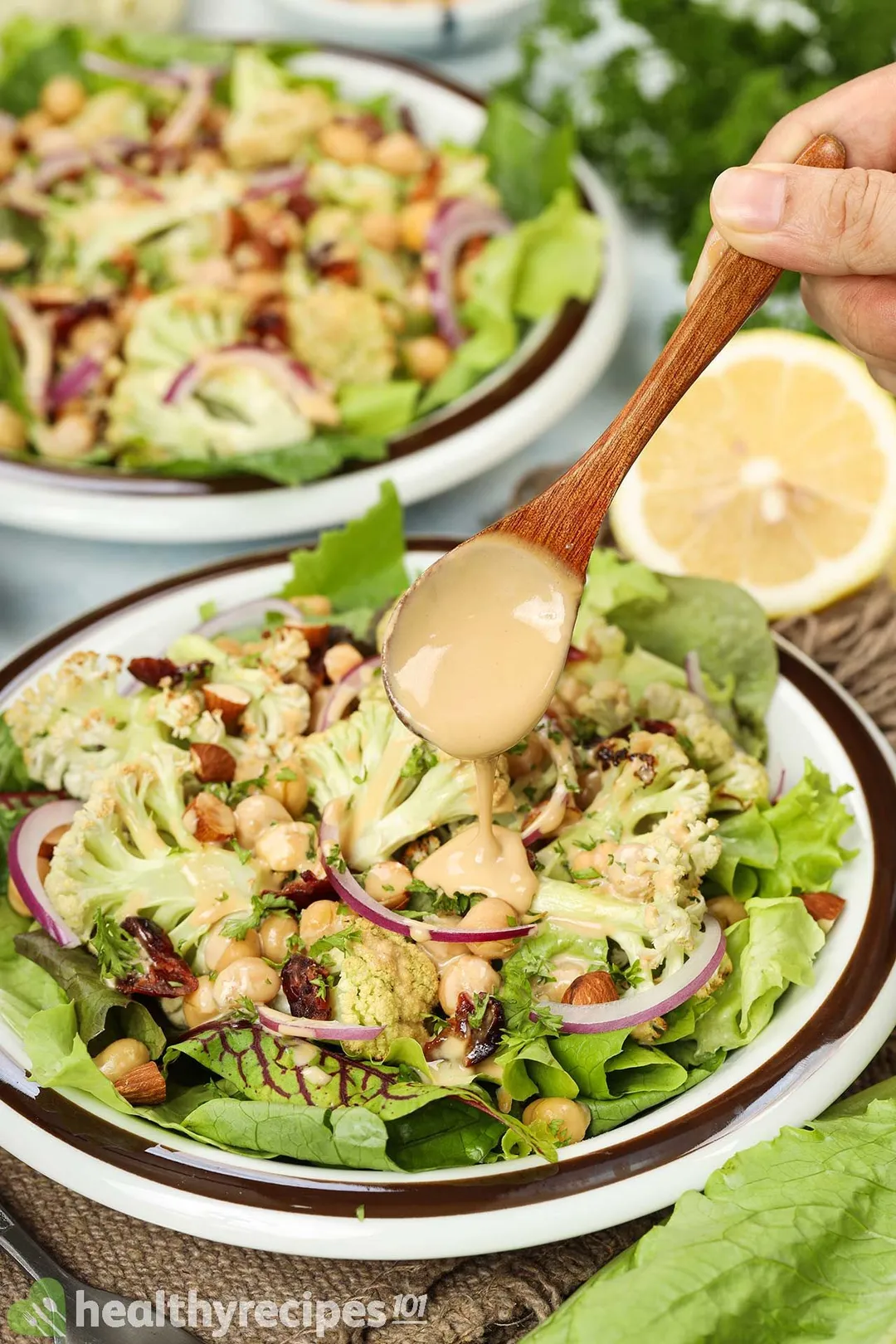 A hand holding a wooden spoon and drizzling a thick orange sauce onto a plate of roasted cauliflower salad