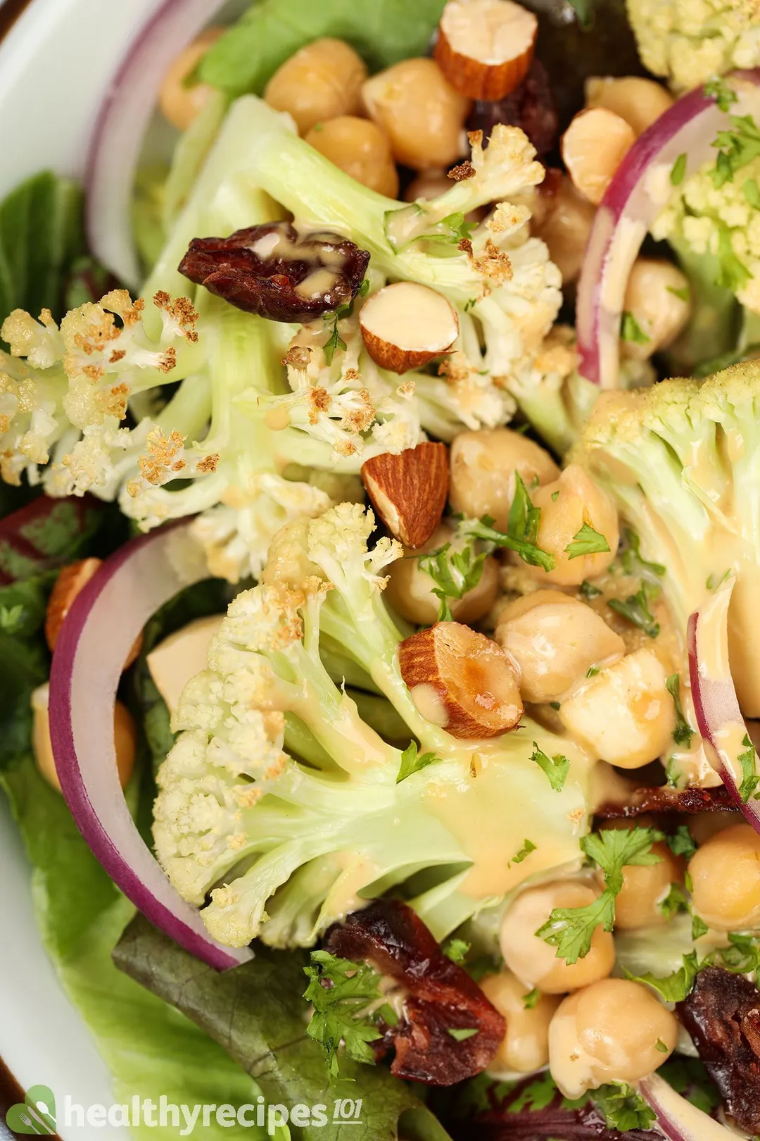 A close-up shot of a roasted cauliflower salad consisting of cauliflower florets, chickpeas, red onion slices, and dried cranberries