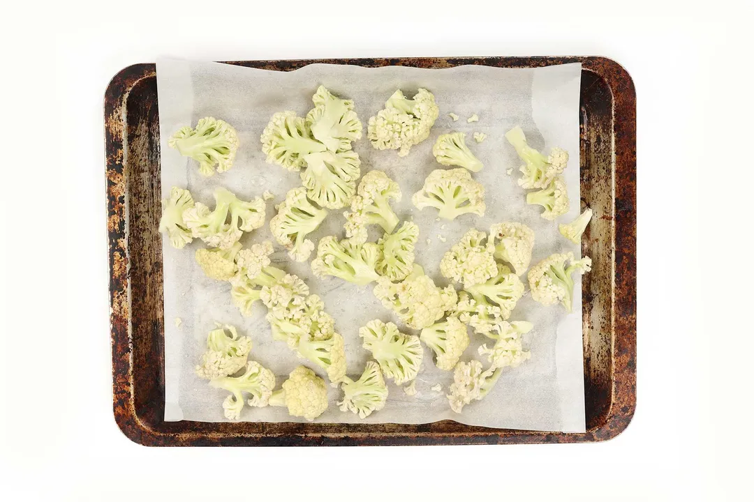 A baking sheet lined with parchment paper and have cauliflower florets spread all over the surface