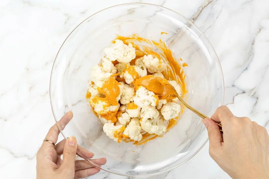 hand holds a spoon to coat cauliflower florets with sauce