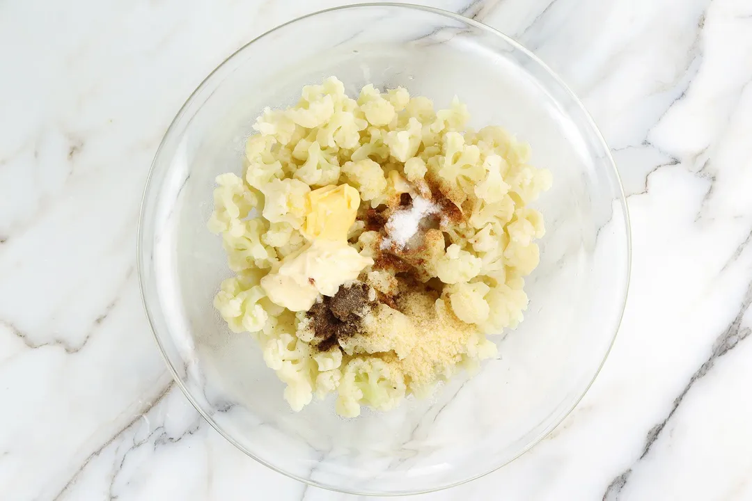 cooked cauliflower florets and seasoning in a glass bowl