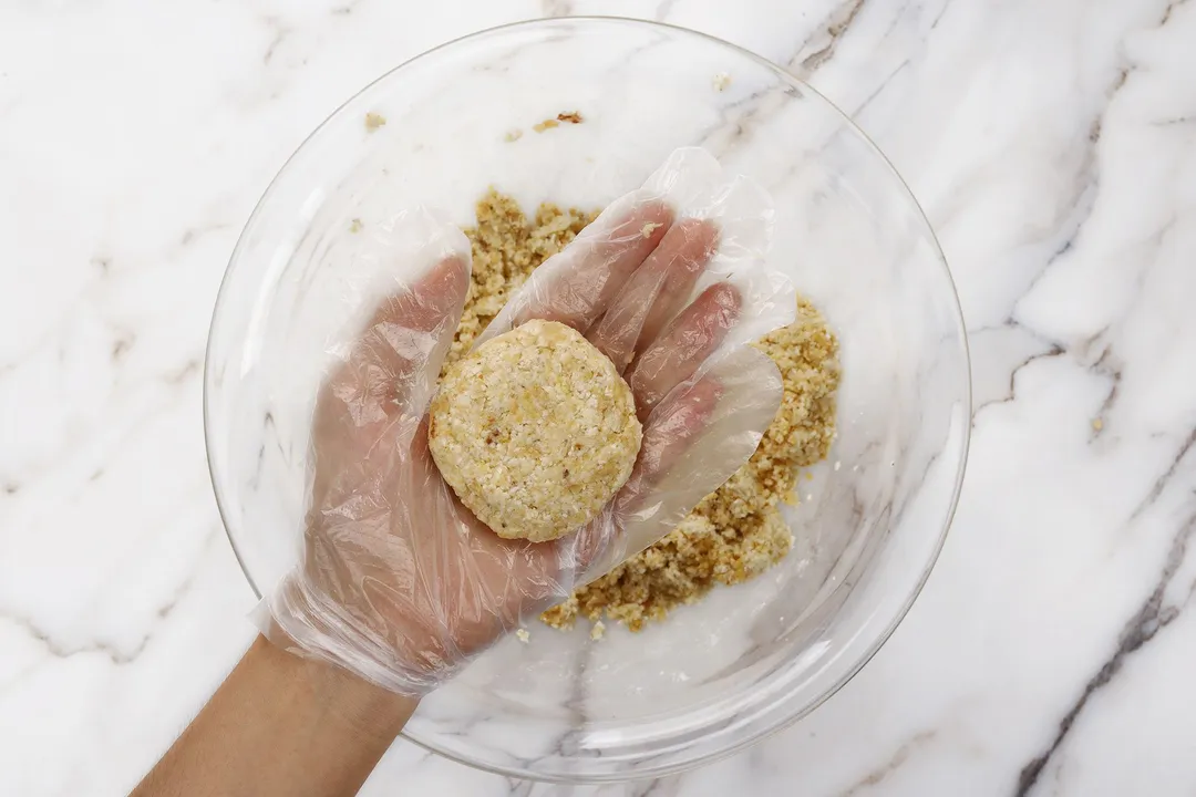 hand holding a patty on top of a glass bowl