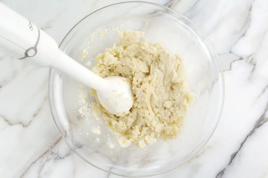 an immersion blender blending cauliflower in a glass bowl