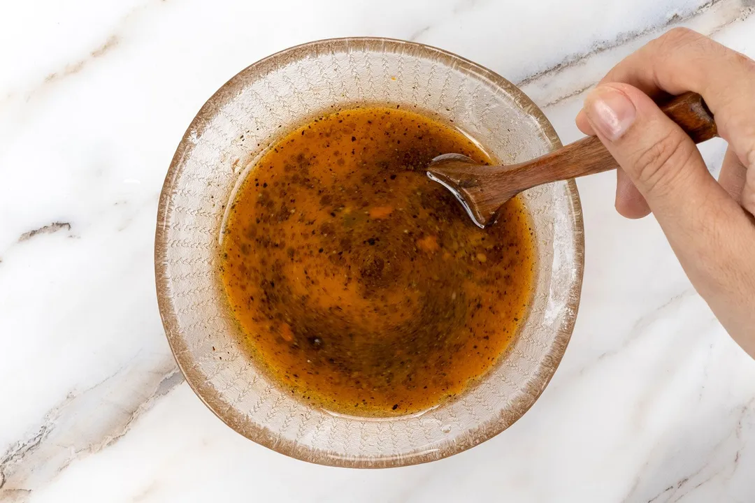 hand hold a spoon to whisking sauce in a glass bowl