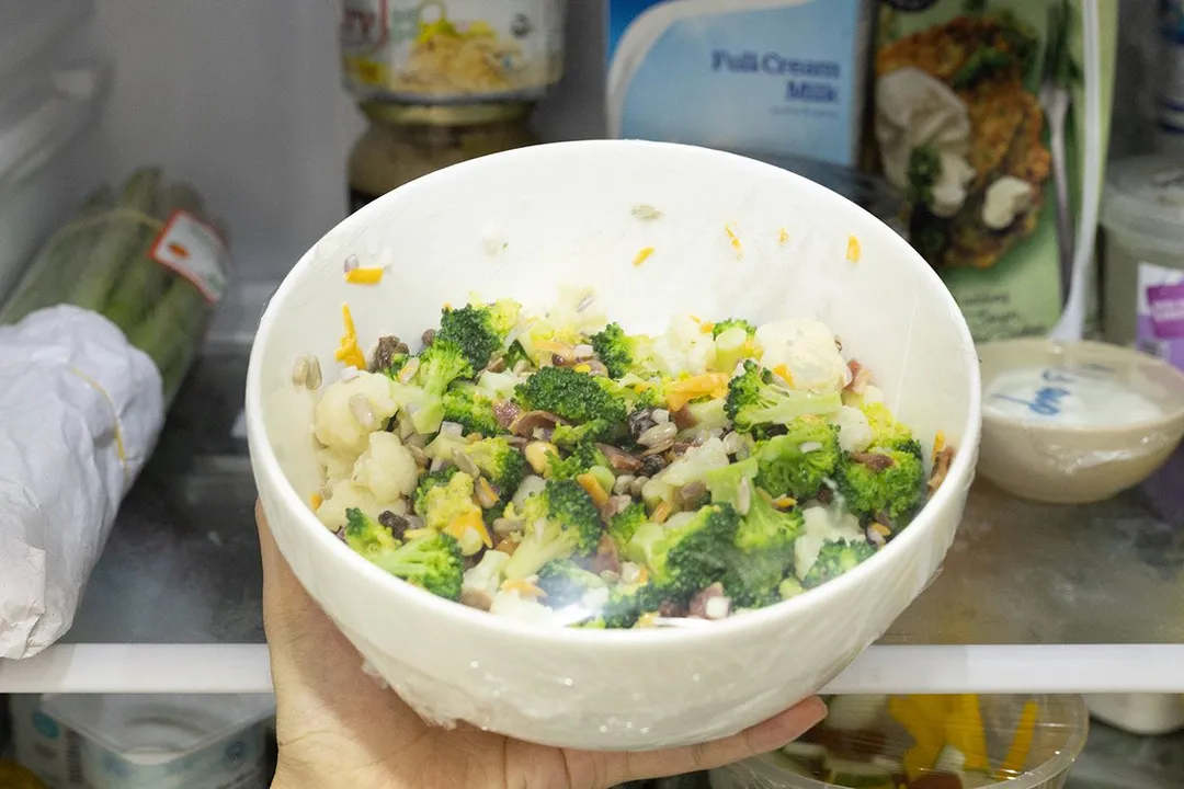 hand holds a bowl of salad in a fridge