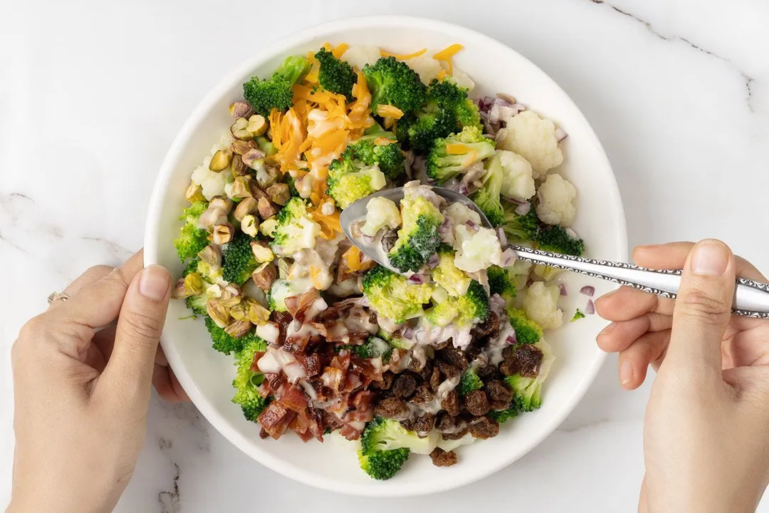 hand holds a spoon on top of a salad plate