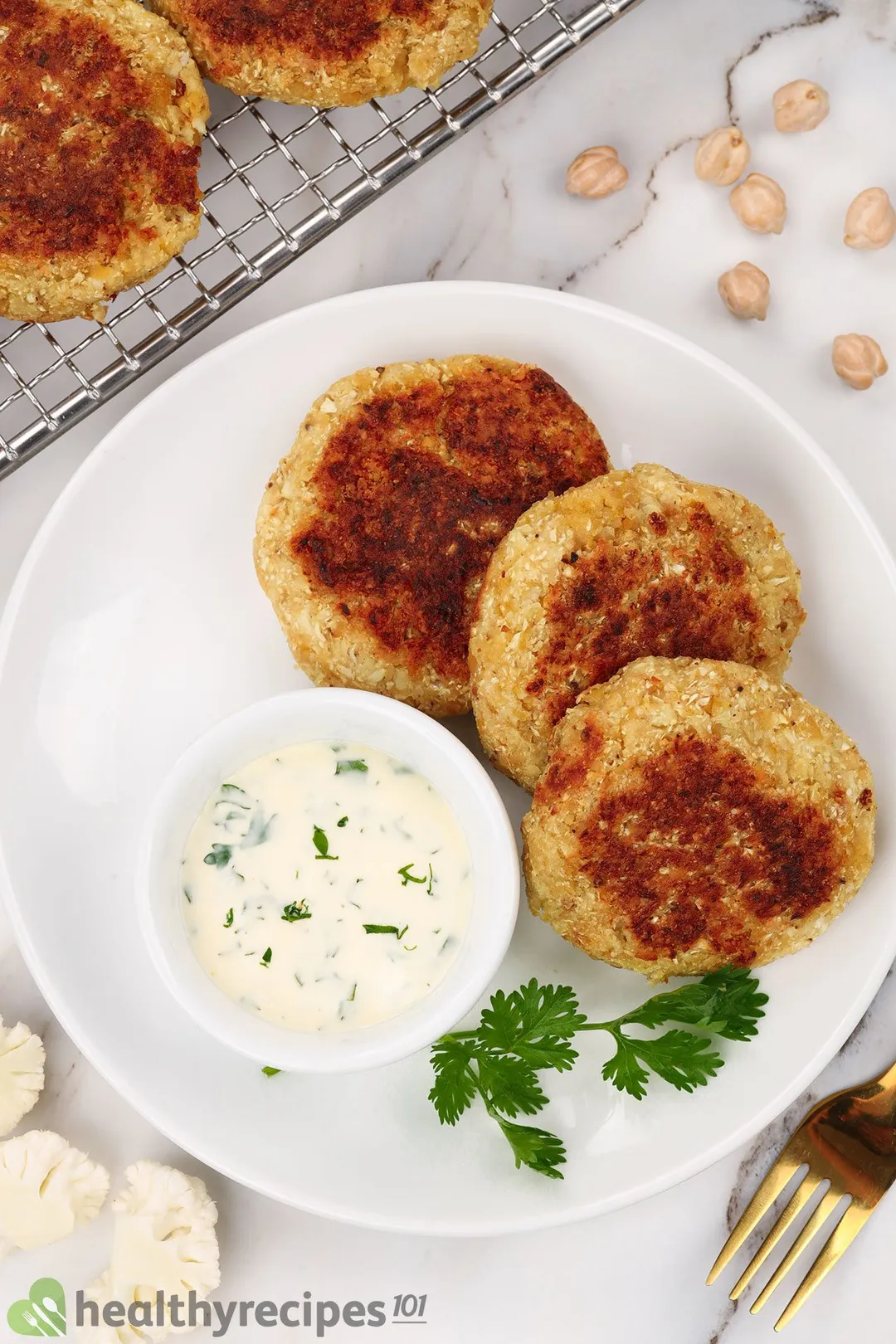 three cauliflower patties on a plate with a small bowl of sauce