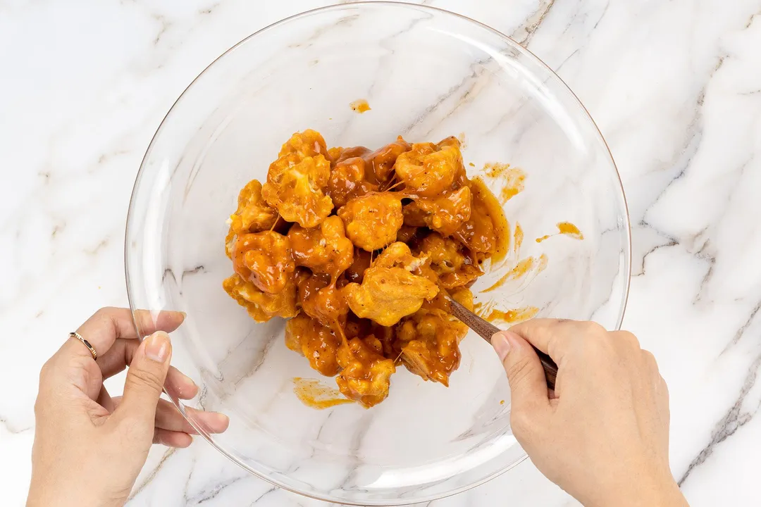 toss coated cauliflower florets with sauce in a glass bowl