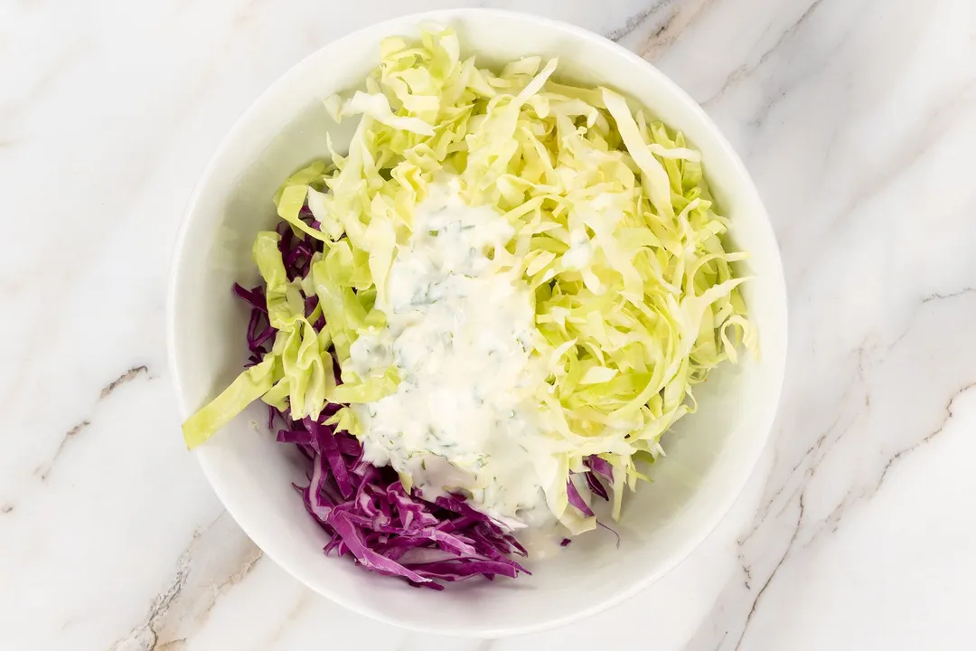 a bowl of shaved green and red cabbage with white dressing in a bowl