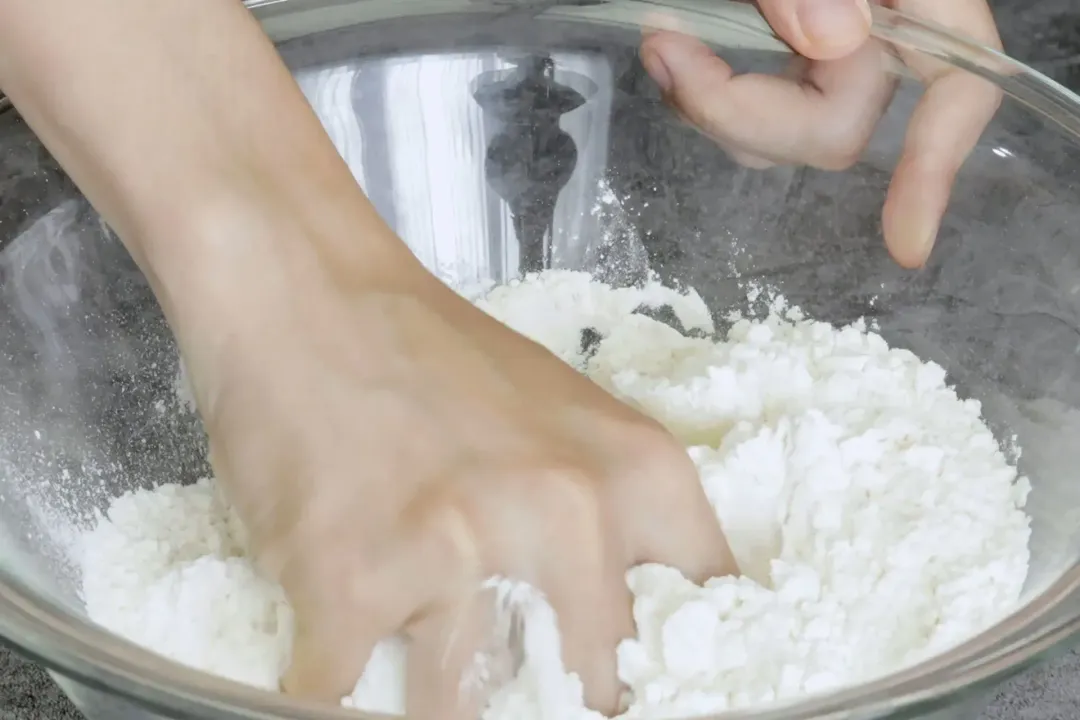 A hand mixing together a bowl filled with white flour