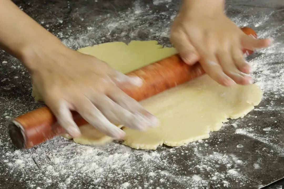 A hand using a rolling pin to flatten a dough