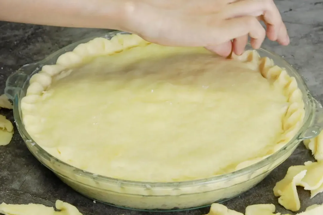A hand pinching the edges of the dough of a chicken pot pie.