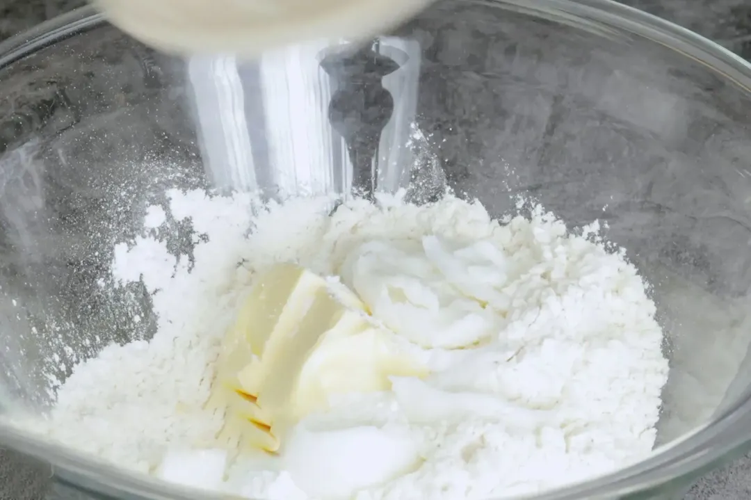 A large white glass bowl containing flour, butter, and other baking essentials
