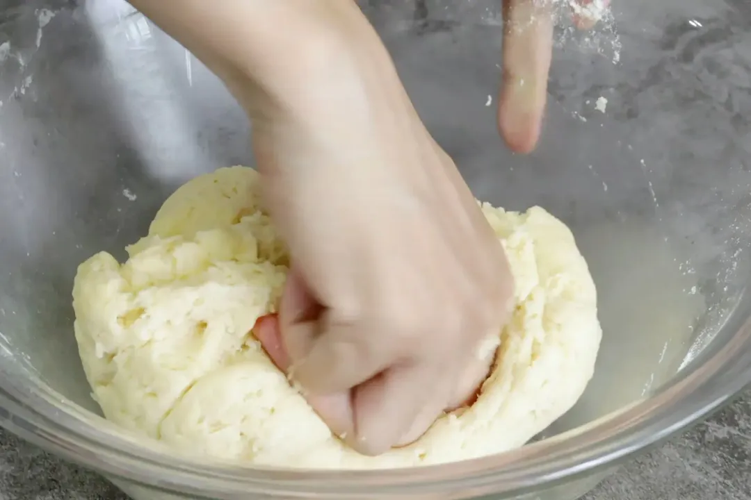 A hand mixing a dough in a large glass bowl