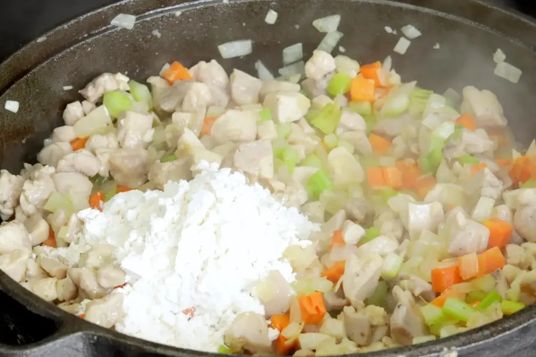 A pot cooking diced carrots, diced onion, and diced celery with a pile of all-purpose flour in the middle