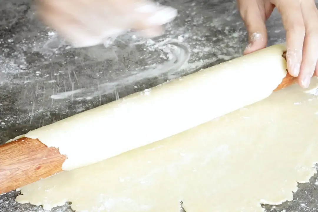 A hand using a rolling pin to roll the dough