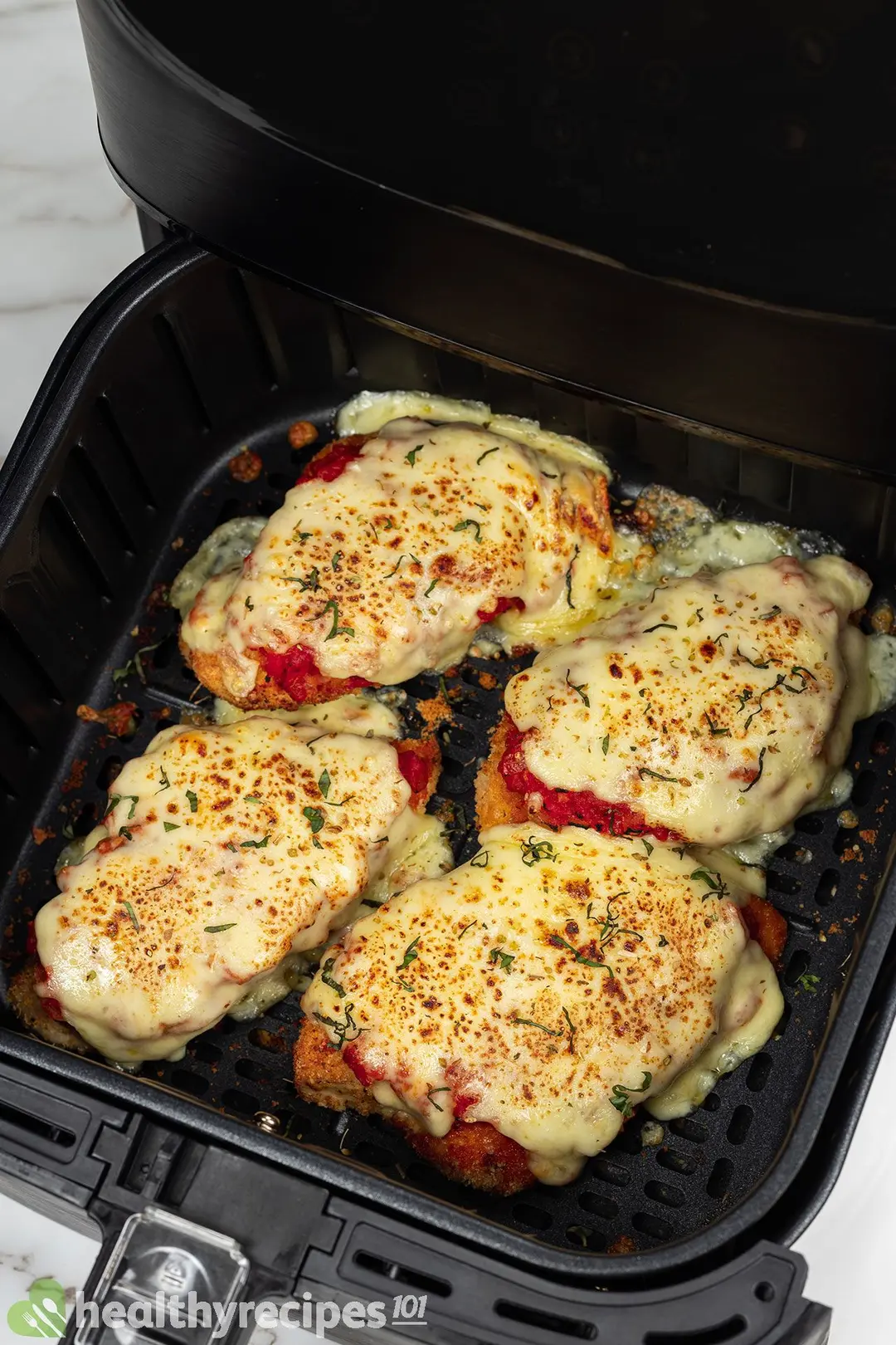 four cooked chicken breasts with mozzarella cheese on top in an air fryer