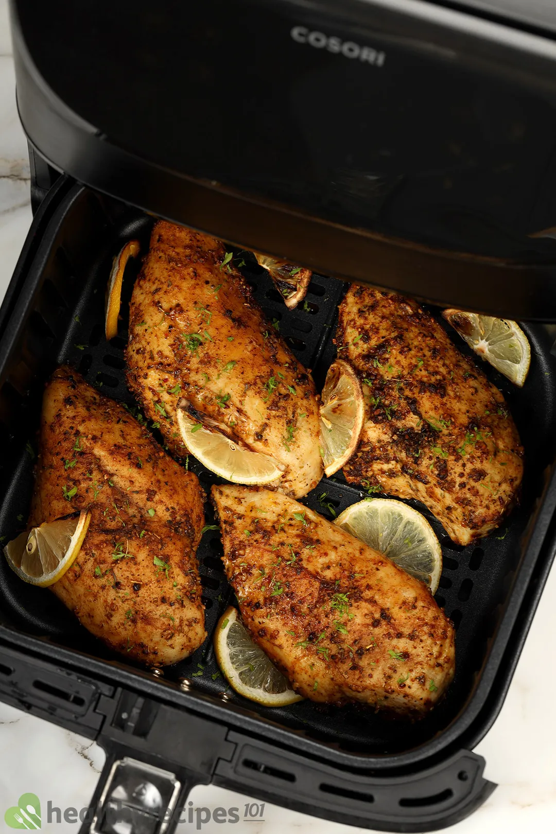 four cooked chicken breasts with lemon slices in an air fryer basket