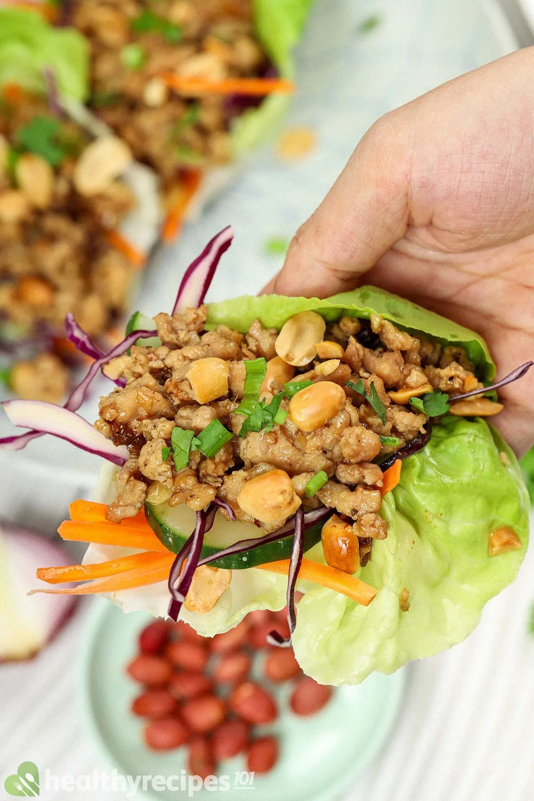 A hand holding a lettuce leaf filled with ground meat, julienned carrots, shredded red cabbage, and peanuts