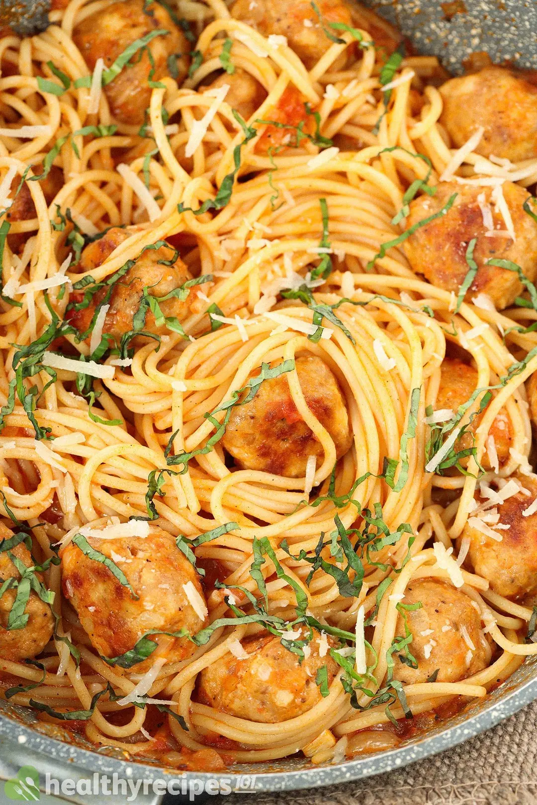 A close-up shot of chicken meatballs with spaghetti, shredded cheese, and parsley