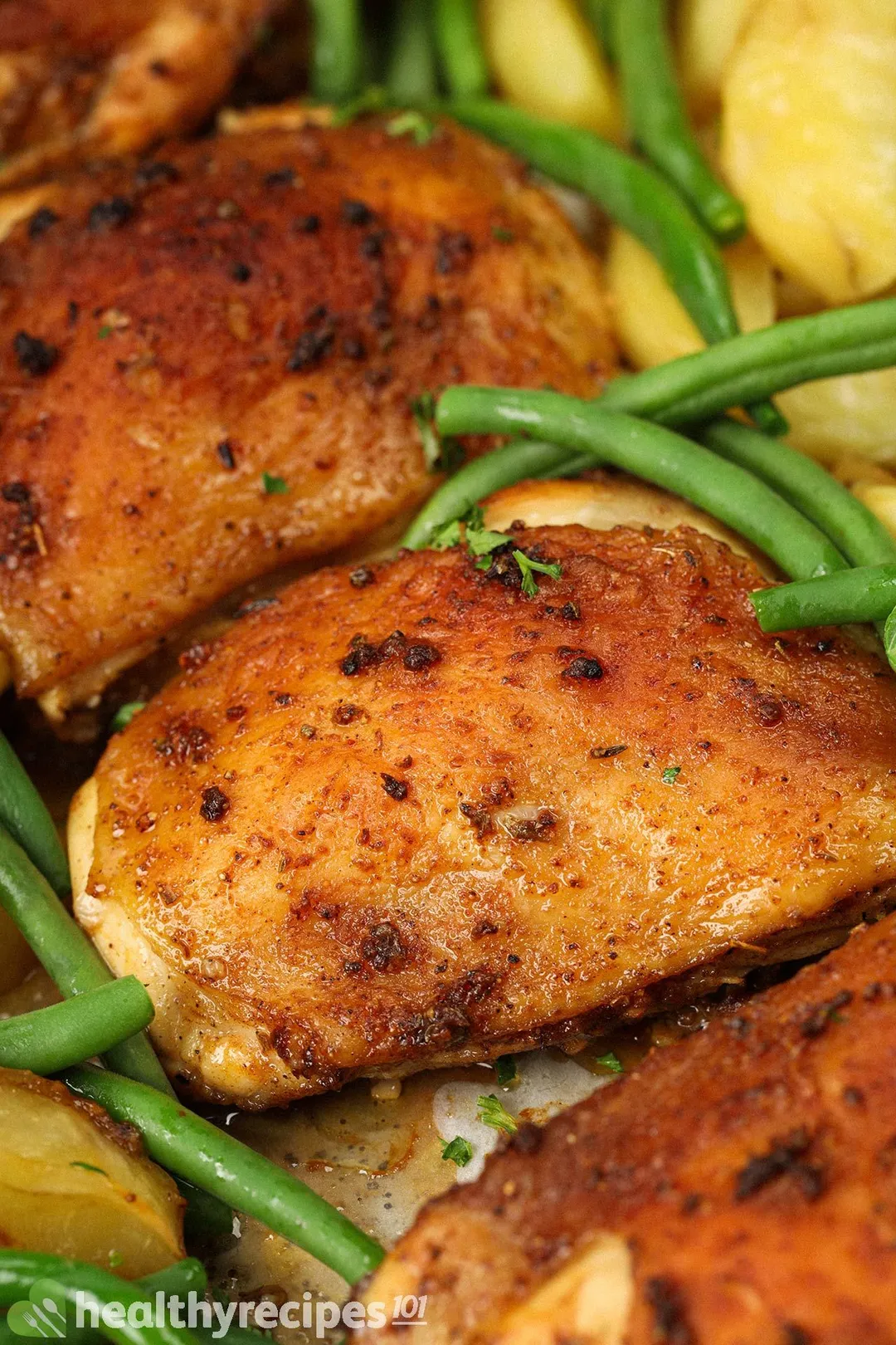 close-up shot of baked chicken thighs on baking tray with green beans and cubed potatoes