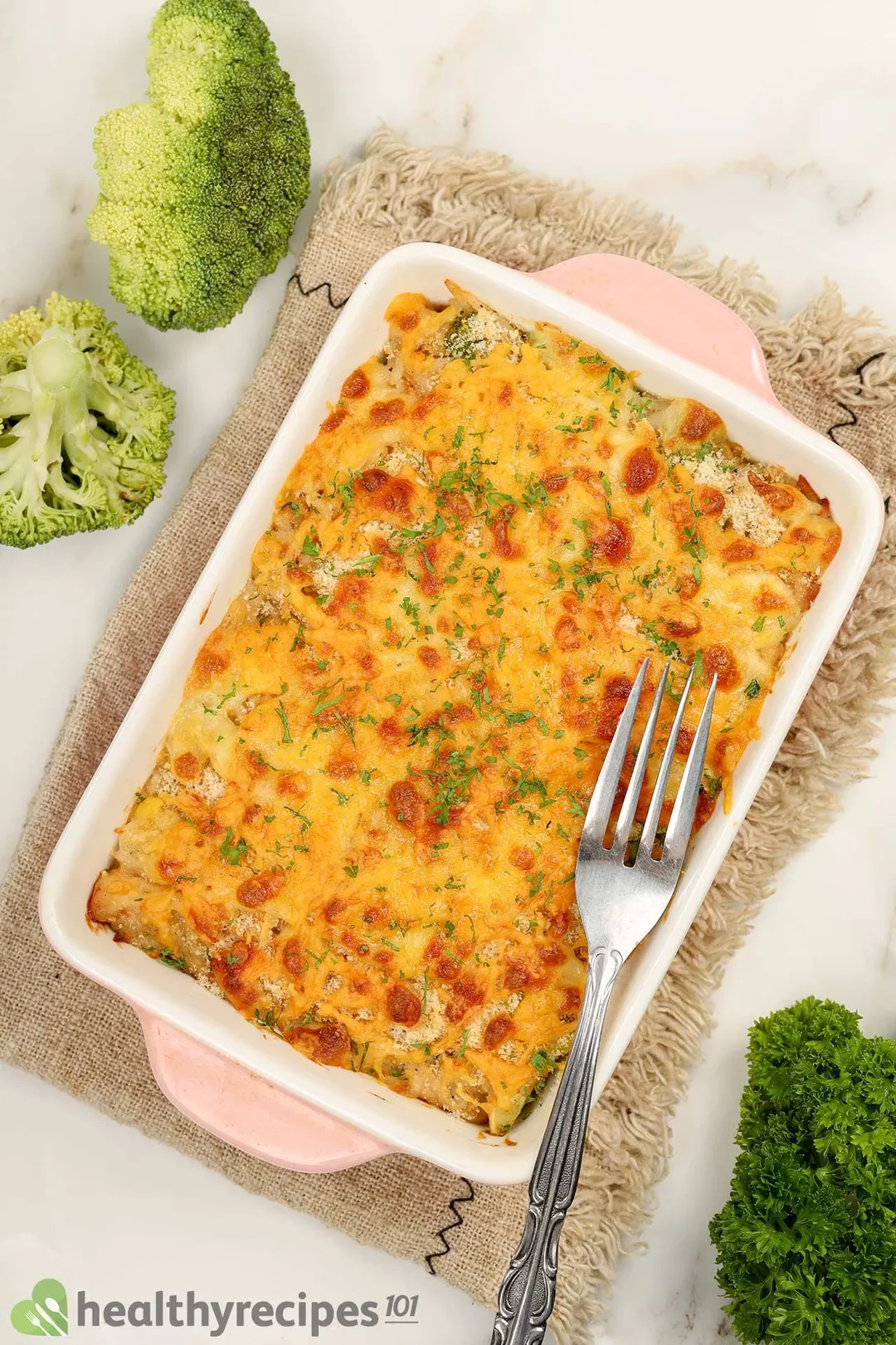 a casserole of cooked chicken broccoli rice with cheese on top, decorated with broccoli, parsley and a fork