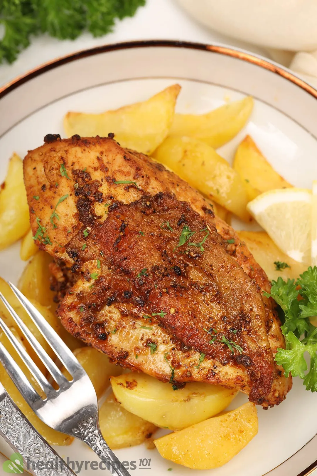 a plate of grilled chicken breast bedding on wedges potatoes, decorated with cilantro and a fork