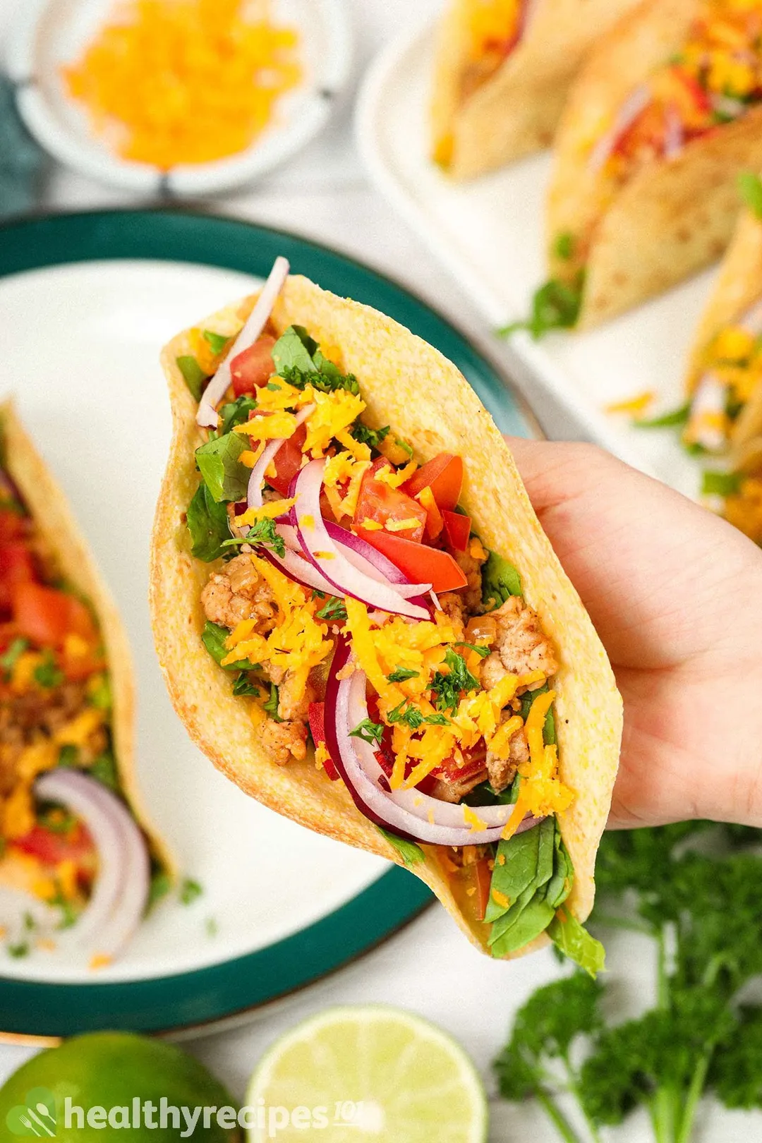 a hand holding a taco with cooked ground chicken anh shredded cheese, sliced onion, pepper, cilantro