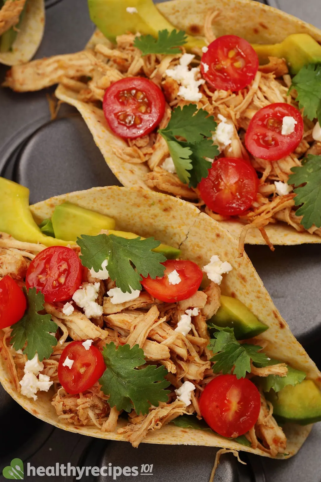 two tacos with shredded chicken and half cherry tomatoes, sliced avocado and cilantro for garnish