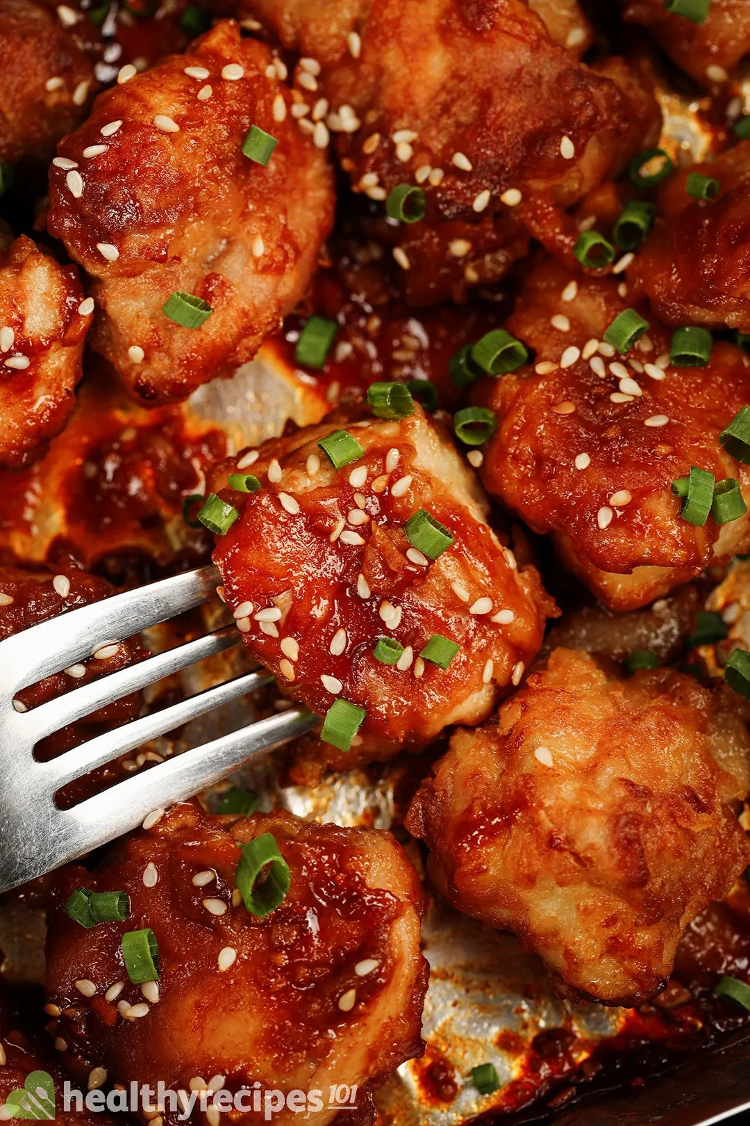 close-up shot of cooked Boneless Skinless Chicken Thigh cubed with a fork, garnished with chopped scallion and sesame seeds