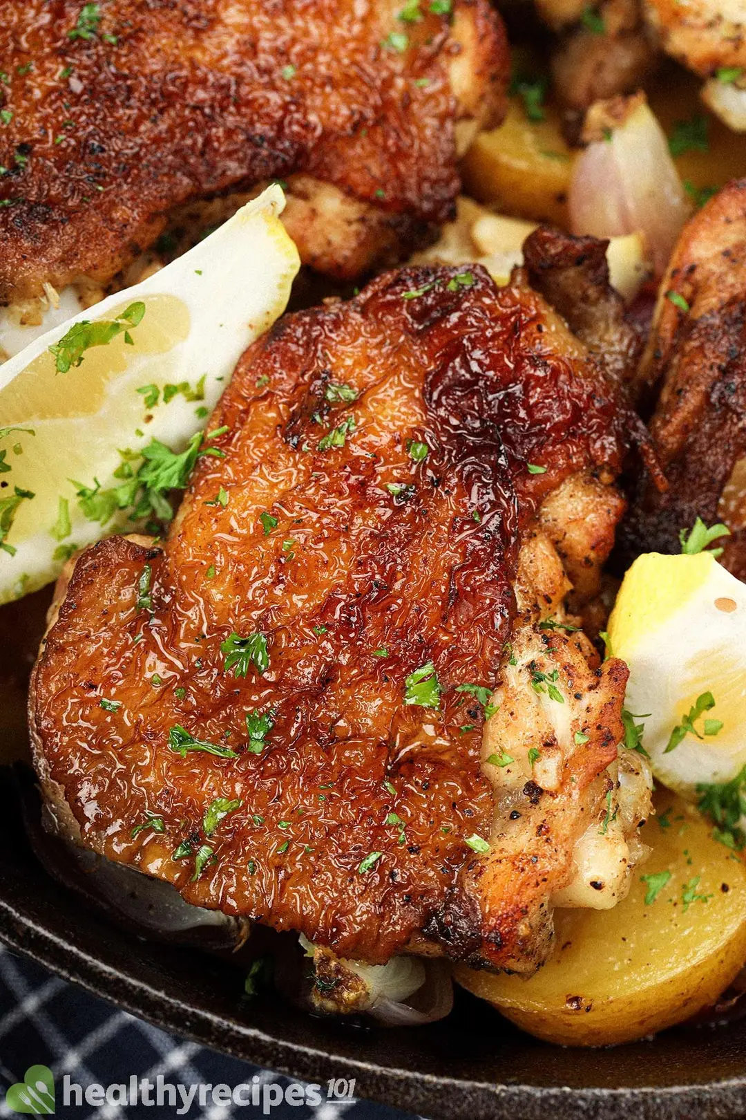 A close-up shot of cooked chicken thighs with browned and glossy skin, laid near cooked baby potatoes