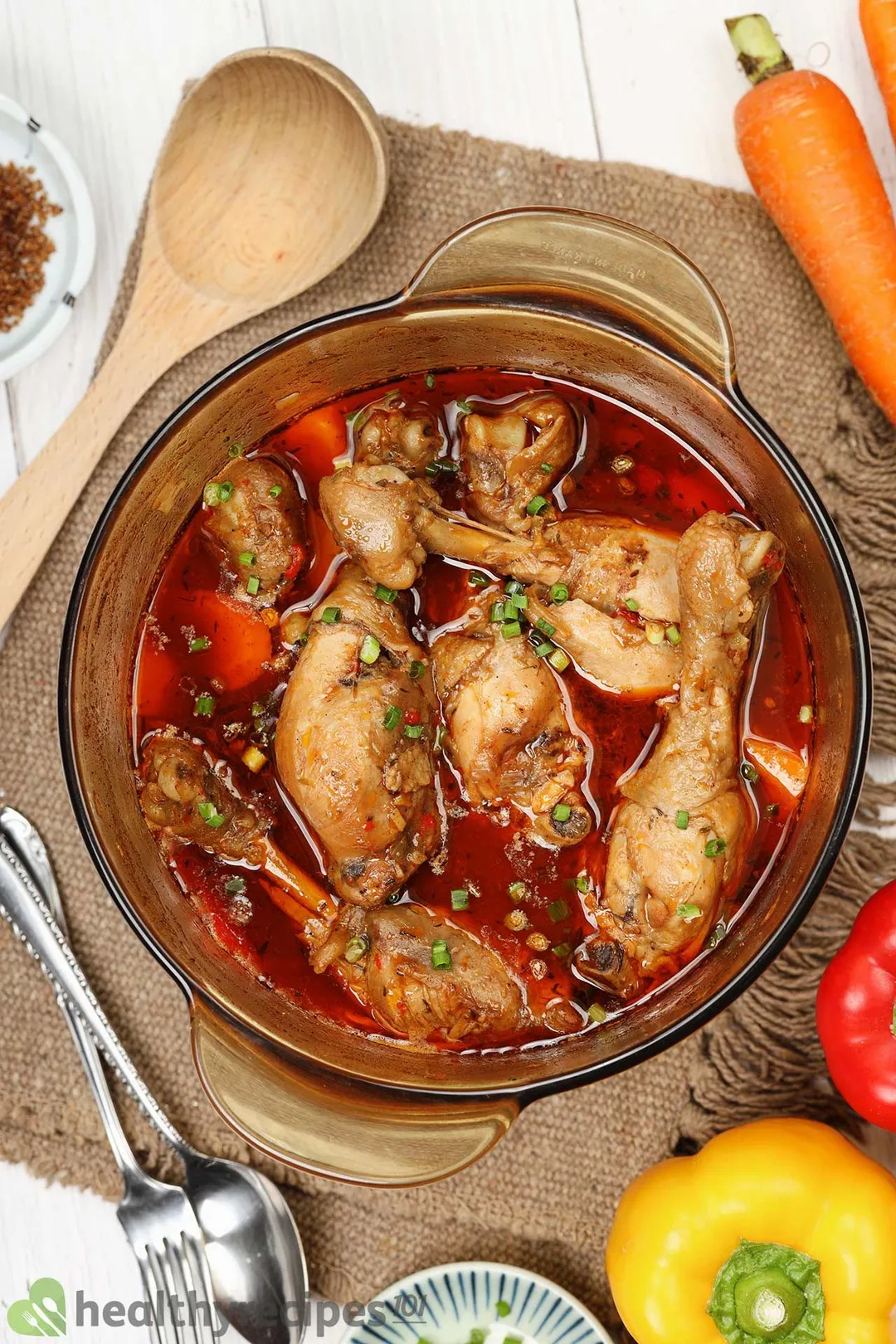 A saucepan containing cooked chicken drumsticks and chopped scallions in a brown stew sauce